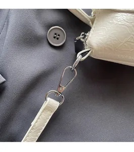 Détail du crochet métallique argenté brillant sur un sac seau en cuir blanc texturé