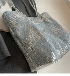 Detail of light blue denim tote bag with silver sequin stripes and grey leather trim