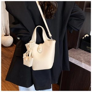 Detail view of the cream lychee grain bucket bag with matching mini charm on a model