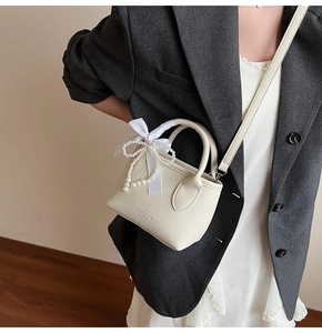 Detail of cream mini bucket bag with silk bow and pearl charms worn with a grey blazer
