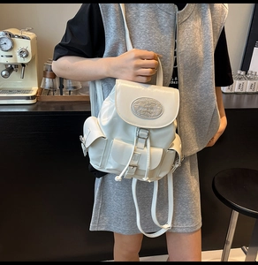 Detail of white mini patent leather backpack with silver metallic logo and drawstring closure