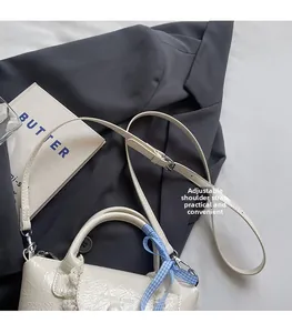 Détail du sac seau en cuir verni blanc avec nœud à carreaux bleus et bandoulière
