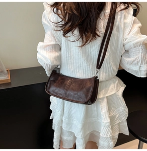 Detail of dark brown vintage leather crossbody bag with silver hardware on female model