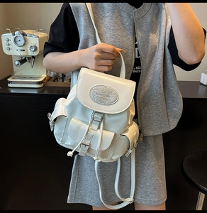 Detail of white glossy backpack featuring silver logo plaque and side pocket drawstring