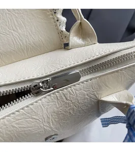 Détail du cuir plissé crème avec fermeture éclair argentée et nœud en ruban bleu