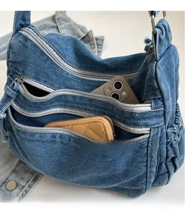 Detail of blue denim shoulder bag showing zipper compartments with phone and wallet inside
