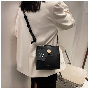 Detail of black crossbody bucket bag featuring floral charm and ruffled shoulder strap