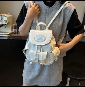 Detail of white leather backpack showing drawstring closure and front buckle pockets