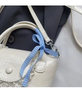 Détail du sac seau en cuir plissé blanc avec bordure en dentelle et nœud à carreaux bleu