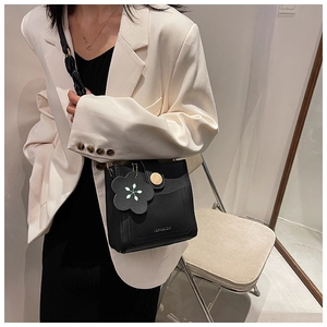 Detail of a chic black crossbody bag with decorative stitching and flower charm on white blazer