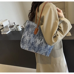 Detailed side view of a large denim tote bag with blue and white pixel pattern and brown straps