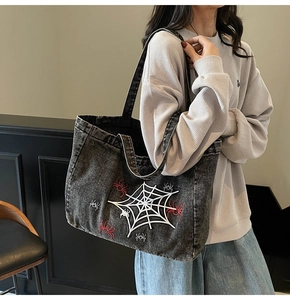 Detailed view of white spider web embroidery on a washed grey denim gothic tote bag
