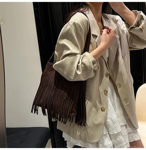 Detail einer dunkelbraunen Wildleder-Beuteltasche mit langen Fransen und Blazer