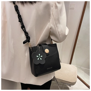 Fashionable black bucket bag with a flower charm and unique twisted shoulder strap detail