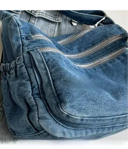 Detail of blue denim tote bag showing multiple zipper pockets and side drawstring compartment