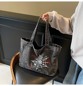 Detail of gothic spider web and red spider embroidery on black washed denim tote bag
