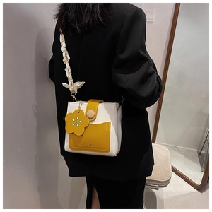 Detail of a contrast color square bag with a large yellow flower charm and woven strap