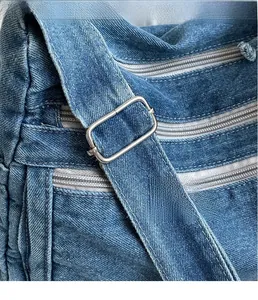 Detail of silver metal buckle and reinforced stitching on blue denim crossbody tote bag