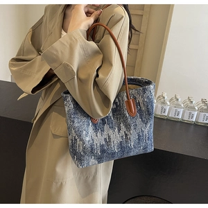 Detail of blue and white woven denim tote bag with brown leather shoulder strap on model