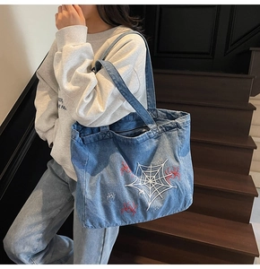 Close-up of white spider web embroidery and red spider motifs on vintage denim tote bag