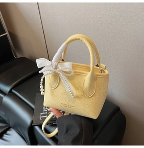 Detail of light yellow mini bucket bag with lychee texture and pearl bow charms