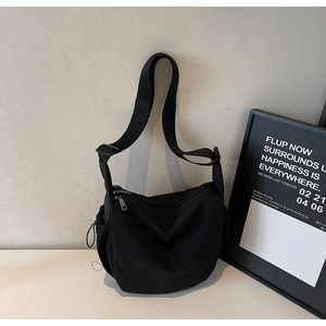 Detail view of black nylon messenger bag featuring multiple zippers and adjustable strap