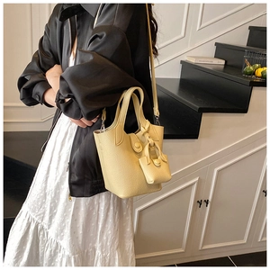 Close-up of creamy yellow lychee grain leather bucket bag with matching mini pouch charm