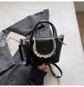 Détail du mini sac seau noir brillant avec bordure en dentelle blanche et nœud à carreaux