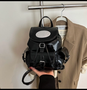 Detail view of black glossy patent leather backpack with silver metallic buckles and logo