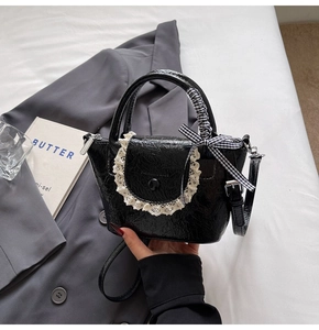 Détail du sac seau en cuir verni noir avec dentelle blanche et nœud à carreaux