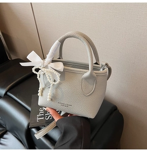 Detail of light grey lychee texture handbag featuring white satin bow and pearl charm