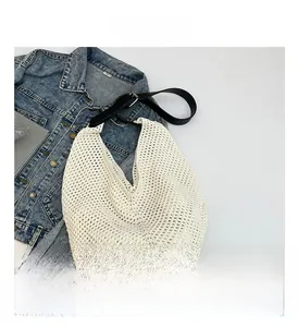 Detail of hollow knit hobo bag with adjustable black leather strap on denim background