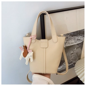 Detail view of cream leather bucket bag with pebble grain texture and horse charm