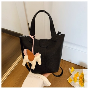Detail of minimalist black pebbled leather bucket bag with a stylish horse charm pendant