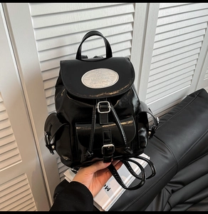 Detail of glossy black leather backpack featuring metallic buckles and multiple pockets