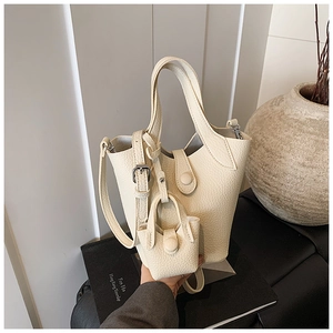 Detail of cream lychee texture leather bucket bag with mini charm on a marble display