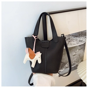 Detail of black lychee grain leather bucket bag with a colorful horse charm accessory