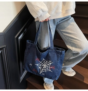 Detailed shot of dark blue denim tote bag featuring gothic white spider web embroidery