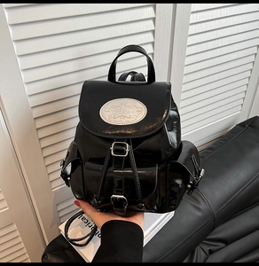 Detail of glossy black patent leather backpack with silver buckle and logo badge
