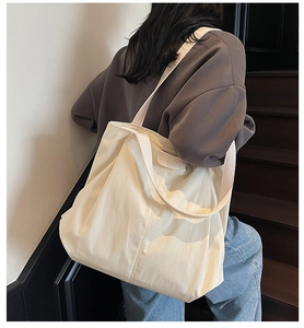 Close-up of cream canvas tote bag with side logo tag worn by model in street setting