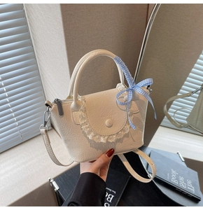 Détail du sac seau blanc cassé avec bordure en dentelle, similicuir plissé et ruban bleu