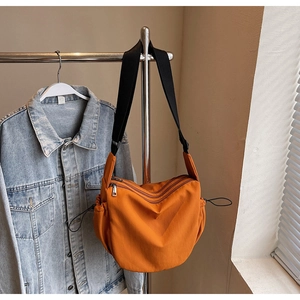 Detailed view of orange hobo bag with multiple zippers and adjustable strap