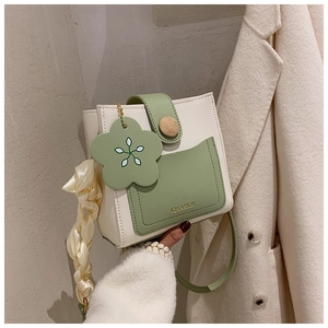 Detailed view of cream and green square crossbody bag with wooden buckle and floral charm