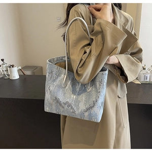 Detailed view of shimmering light blue sequin tote bag with metallic stripes on denim