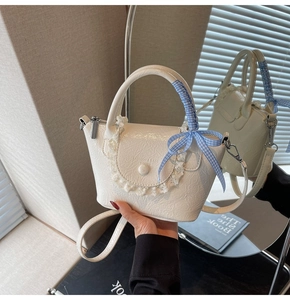 Détail d'un sac seau crème avec bordure en dentelle et poignée ruban à carreaux