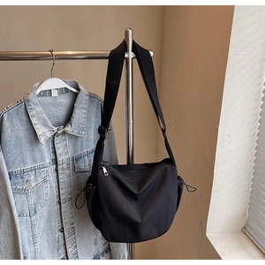 Close-up of black crossbody bag with adjustable wide strap and side drawstring pockets