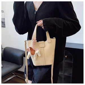 Detailed view of cream leather bucket bag with horse charm and long shoulder strap