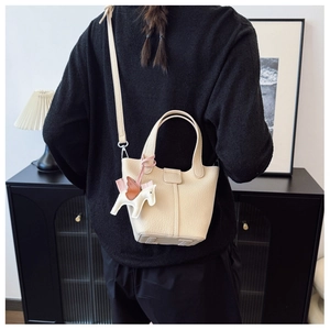 Detail of cream bucket bag with lychee texture leather and a colorful pegasus charm