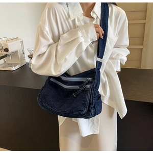 Detail of blue denim crossbody bag with multiple zippers shown on a model