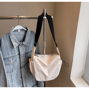 Detail of cream nylon crossbody bag featuring black wide strap and side drawstring accents